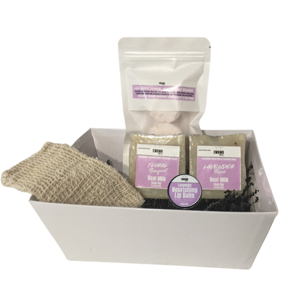 White gift box with skincare products including a scrub, soap, and lip balm on a white background